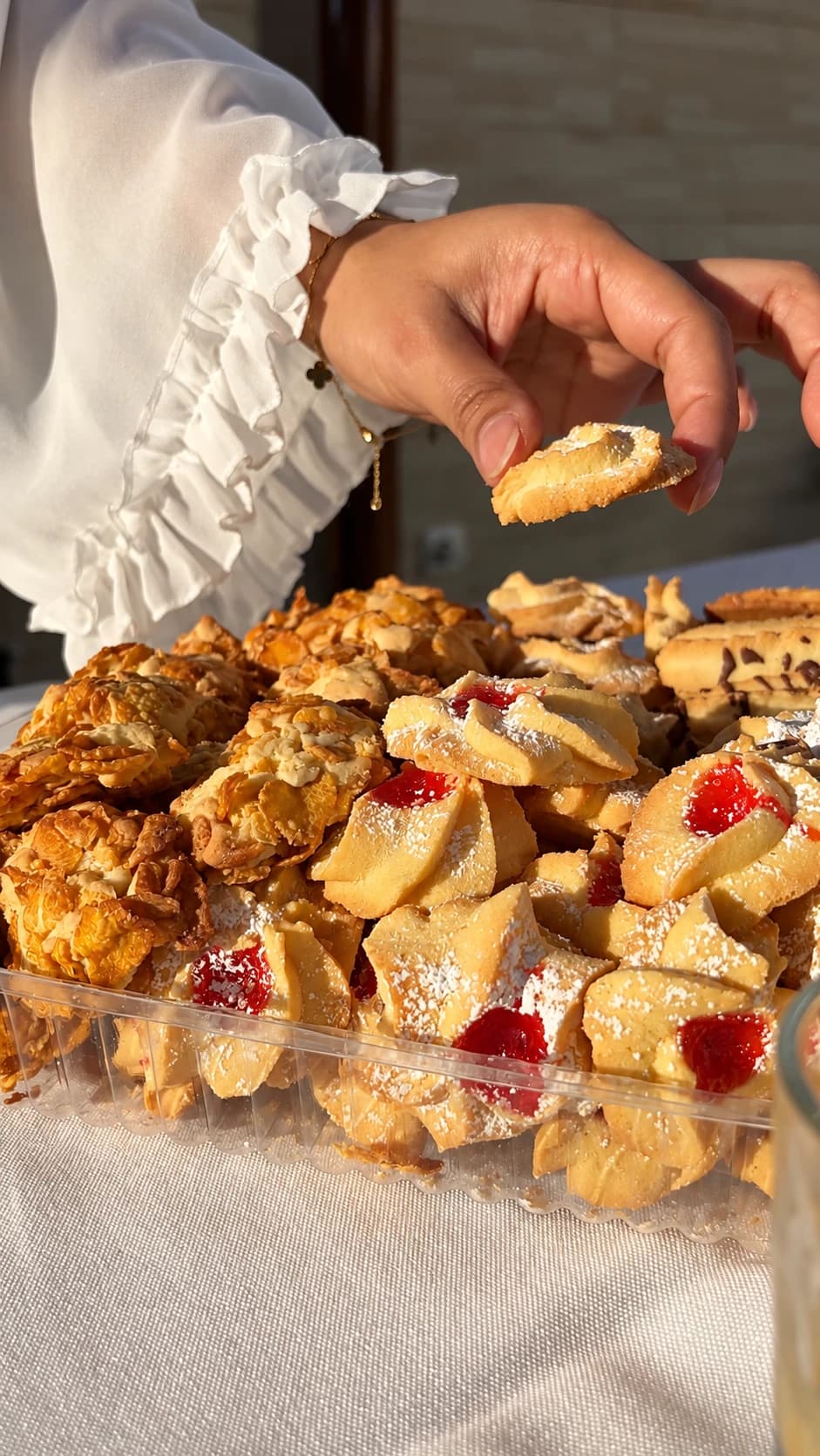 Mão a escolher um biscoito de manteiga numa caixa cheia de biscoitos com doce de morango e flocos crocantes
